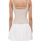 Woman shown from the back wearing the Simkhai Fifi Mini Dress—a sleeveless, light beige linen poplin mini with thin straps and a white, gathered skirt above the knee.