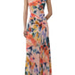 A woman wearing the Simkhai Acacia Jersey Midi Dress, featuring a sleeveless design, multicolored floral print, side ruching, and paired with white heeled sandals.