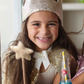 A girl wearing a Great Pretenders Gracious Gold Sequins Crown adorned with sequins.