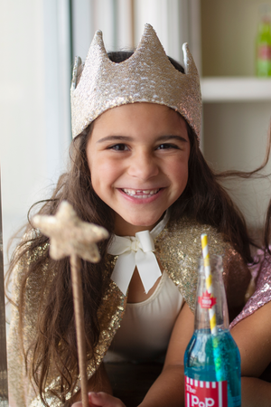 A girl wearing a Great Pretenders Gracious Gold Sequins Crown adorned with sequins.