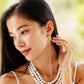 A woman with long dark hair wears Juliska Capucine De Wulf Berry Classic Small Hoop Earrings, touching one earring with her hand as she gazes slightly downward and to the side.