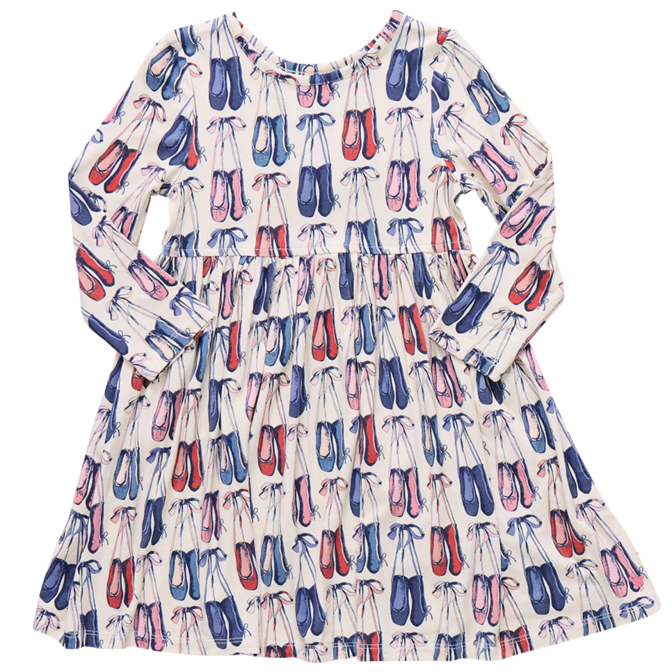 The Girls' Bamboo Steph Dress by Pink Chicken features long sleeves, a gathered waist, and a playful print of pink, red, and blue ballet shoes on soft white bamboo fabric.