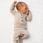 A baby wearing the Lou Lou & Company Baby Boys’ and Boys’ Banks Top & Bottoms sleeps on a white quilted blanket, holding a pacifier near their mouth.