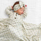 A newborn baby sleeps on a white textured blanket, wearing the Lou Lou & Company Baby Girls’ and Girls’ Etta Top & Bottoms, featuring a matching leafy patterned design and wooden buttons, crafted from silky-soft fabric for ultimate comfort.