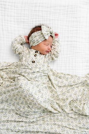 A newborn baby sleeps on a white textured blanket, wearing the Lou Lou & Company Baby Girls’ and Girls’ Etta Top & Bottoms, featuring a matching leafy patterned design and wooden buttons, crafted from silky-soft fabric for ultimate comfort.