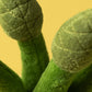 Close-up of green, textured plush fabric shaped like stems and buds, resembling the Amuseables Asparagus by Jellycat, set against a solid yellow background.