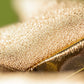 Close-up of golden, textured fabric with a glittery, metallic look, inspired by the dazzling style of Jellycat's Amuseables Zapperty Lightning Bolt plush toy.
