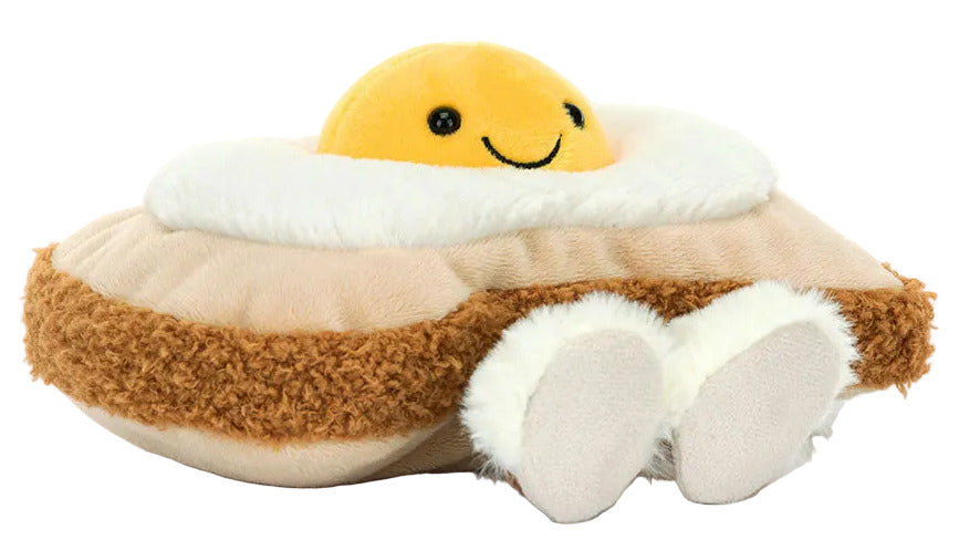 The Jellycat Amuseables Egglantine Egg on Toast is a plush toy shaped like egg on toast, featuring a smiling yellow yolk, white and brown details, and small feet at the bottom.