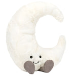 The Jellycat Amuseables Moon plush toy, by Jellycat, is designed in the shape of a crescent moon with a cheerful smiling face and two tiny gray feet, set against a white background.