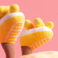 Close-up of Jellycat Amuseables Sun 'Roller Skates' plush’s yellow feet with white embroidered details and brown legs, set against a pink background, ready for boardwalk roller skating fun.