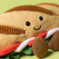 The Jellycat Amuseables Caprese Baguette is a plush toy shaped like a smiling sandwich, featuring brown bread, green lettuce, and colorful fillings, shown on a light green background.
