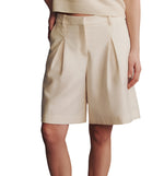 Someone is wearing the TWP St George Shorts, which are beige and mid-rise, paired with a matching top made of cotton linen, with their hands relaxed by their side.