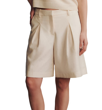 Someone is wearing the TWP St George Shorts, which are beige and mid-rise, paired with a matching top made of cotton linen, with their hands relaxed by their side.