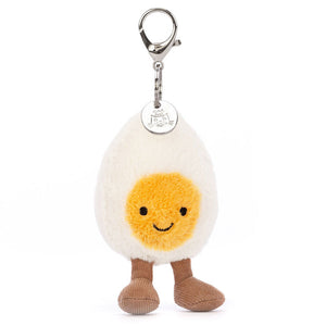 The Jellycat Amuseables Happy Boiled Egg Bag Charm features a smiling egg with a yellow yolk and brown legs, attached to a silver clasp.
