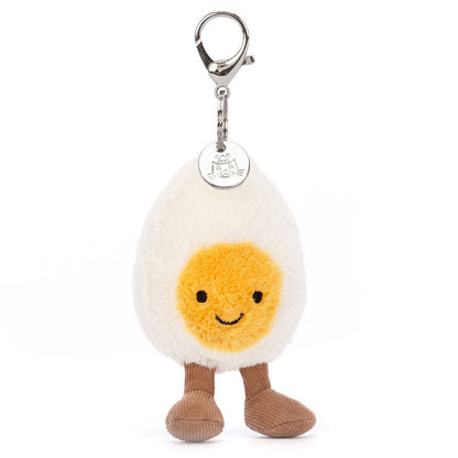 The Jellycat Amuseables Happy Boiled Egg Bag Charm features a smiling egg with a yellow yolk and brown legs, attached to a silver clasp.