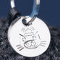 Close-up of the Jellycat Amuseables Black Hole Bag Charm—a round silver tag engraved with a cartoon cat in a hat, attached to a metal ring. Perfect as a quirky physics gift or unique accessory for Jellycat fans.