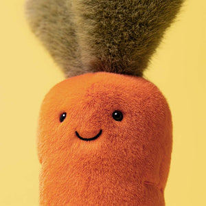 Close-up of the Jellycat Amuseables Carrot plush, featuring a cheerful face, black eyes, and a green leafy top against a yellow background.
