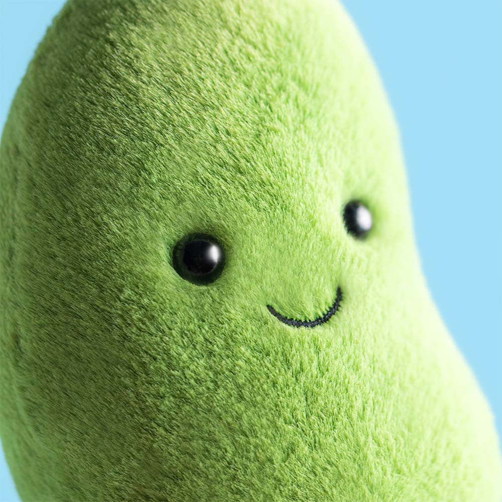 Close-up of the Jellycat Amuseables Soyella Edamame Bean plush toy, featuring a green bean shape with black button eyes and a stitched smile, set against a blue background.