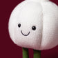 The Jellycat Amuseables Garlic plush toy features a cheerful smiling face and green legs, all in the shape of a garlic bulb. Set against a solid dark red background, it’s the perfect whimsical accent for your Halloween party decor.