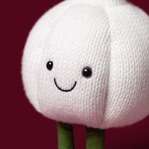 The Jellycat Amuseables Garlic plush toy features a cheerful smiling face and green legs, all in the shape of a garlic bulb. Set against a solid dark red background, it’s the perfect whimsical accent for your Halloween party decor.