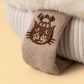 Close-up of a beige fabric tag with a brown embroidered cat face on a cream ribbed textile from Jellycat’s Amuseables Fitswell Mitten.