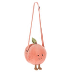 The Jellycat Amuseables Peach Shoulder Bag features a long pink strap, green felt leaf, small legs, and a smiling face.