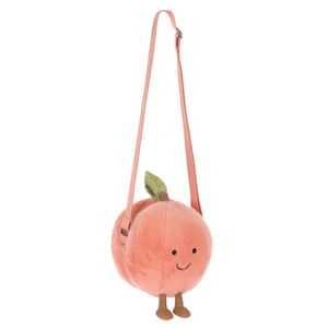 The Jellycat Amuseables Peach Shoulder Bag features a long pink strap, green felt leaf, small legs, and a smiling face.