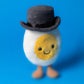 Meet the Jellycat Amuseables Boiled Egg Groom: a whimsical plush toy shaped like a fried egg with a smiling face, black top hat, and two small legs, perfect for adding charm to any collection.