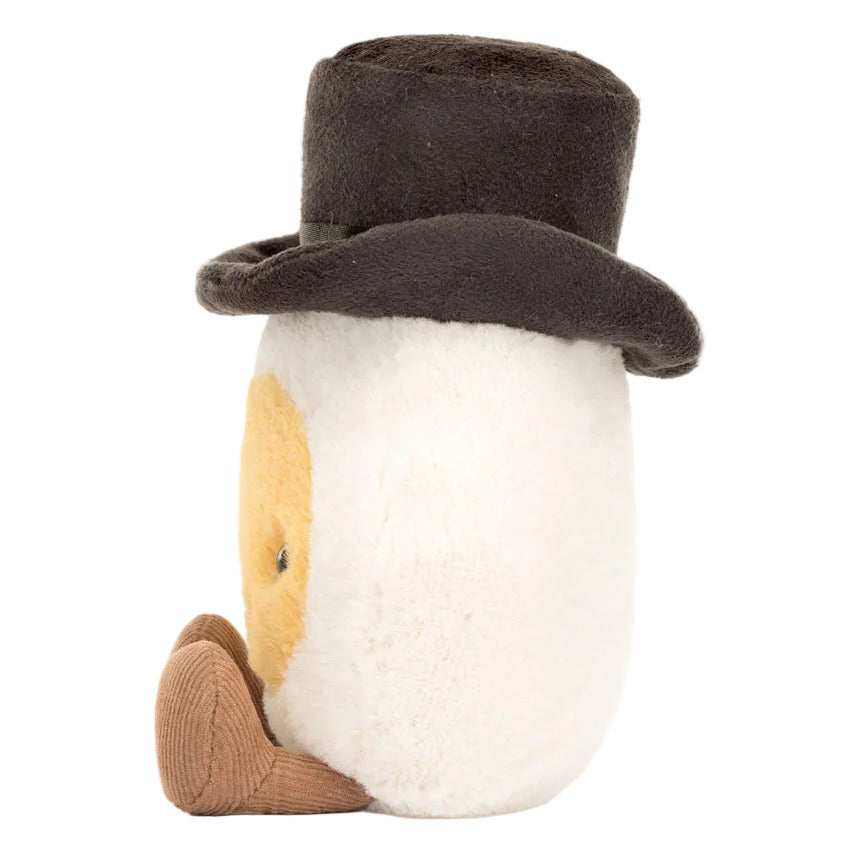 Meet the Jellycat Amuseables Boiled Egg Groom, a plush toy shaped like an egg with a yellow face, stylish black top hat, and brown shoes, pictured on a white background.