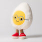 The Jellycat Amuseables Boiled Egg Geek is a plush toy shaped like a smiling fried egg with round glasses, brown legs, and red shoes—an adorable and quirky stuffed toy for any collection.