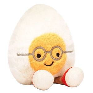 The Jellycat Amuseables Boiled Egg Geek is a plush toy shaped like a half egg with a yellow center, embroidered glasses, a smile, and red and white feet, shown on a plain background.
