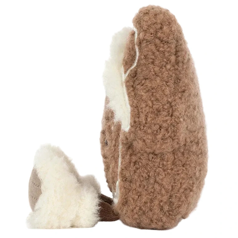 Side profile of a brown, fuzzy, round Jellycat Amuseables Molasi Cookie with white cream filling and dangling plush legs.
