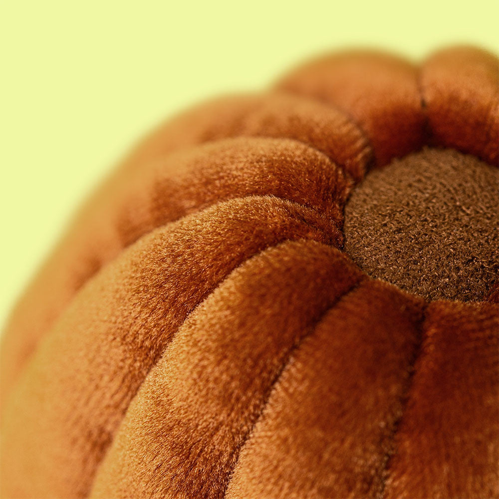 Close-up of the Amuseables Carole Canele from Jellycat, featuring plush orange velvet-like fabric and a brown stem, set against a pale yellow background.