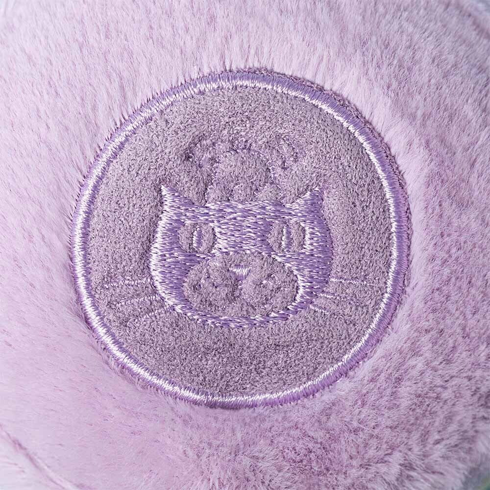 A close-up of a round, embroidered purple patch with a stylized cat face on soft lavender fabric, inspired by the Jellycat Amuseables May Macaron - Lavender plush toy.
