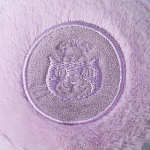 A close-up of a round, embroidered purple patch with a stylized cat face on soft lavender fabric, inspired by the Jellycat Amuseables May Macaron - Lavender plush toy.