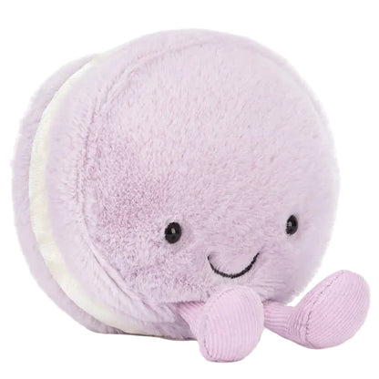 The Jellycat Amuseables May Macaron - Lavender is a plush toy shaped like a lavender macaron, with a smiling face, black eyes, and two small dangling legs.