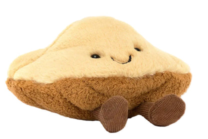 The Jellycat Amuseables Margaux Madeleine is a plush toy shaped like a madeleine with a smiling face and small brown corduroy legs, shown against a white background.