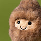 A close-up of the Jellycat Amuseables Peanut Yeti Outfit plush, featuring brown fur, black button eyes, and a stitched smile against a plain green background.