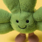 The Jellycat Amuseables Siofra Shamrock is a green leafy plush with a smiling face, black eyes, and brown feet, shown on a vibrant yellow background.