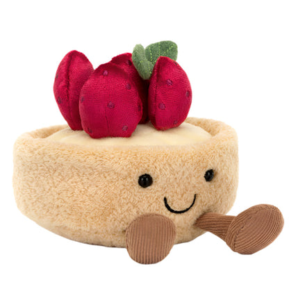 The Jellycat Amuseables Fleurette Tarte Aux Fraises plush toy is a smiling cheesecake shape with red plush strawberries and delightful brown legs.