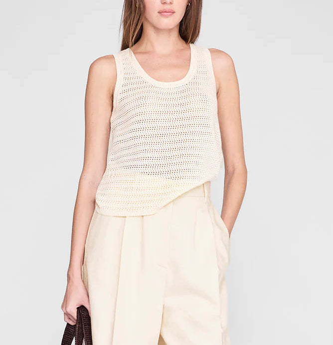 Someone wearing the Arie Tank from Anine Bing—a sleeveless, cream lightweight knit with a scoop neckline—paired with high-waisted light beige trousers and holding a dark brown bag.