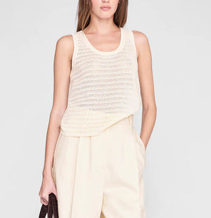 Someone wearing the Arie Tank from Anine Bing—a sleeveless, cream lightweight knit with a scoop neckline—paired with high-waisted light beige trousers and holding a dark brown bag.