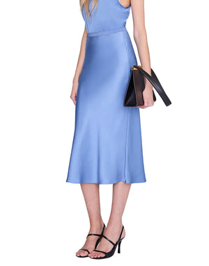 A person wearing the Bar Silk Skirt by Anine Bing, styled as a sleeveless light blue satin midi dress, paired with black heeled sandals and holding a black clutch bag against a white background.