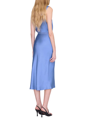 A woman with long blonde hair stands with her back to the camera against a white background, wearing the Anine Bing Bar Silk Skirt in light blue as a midi-length dress paired with black heeled sandals.