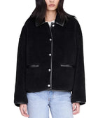 A person wearing the Camden Jacket by Anine Bing—a black, button-up wool blend workwear jacket with leather trim—paired with light blue jeans, standing against a white background.