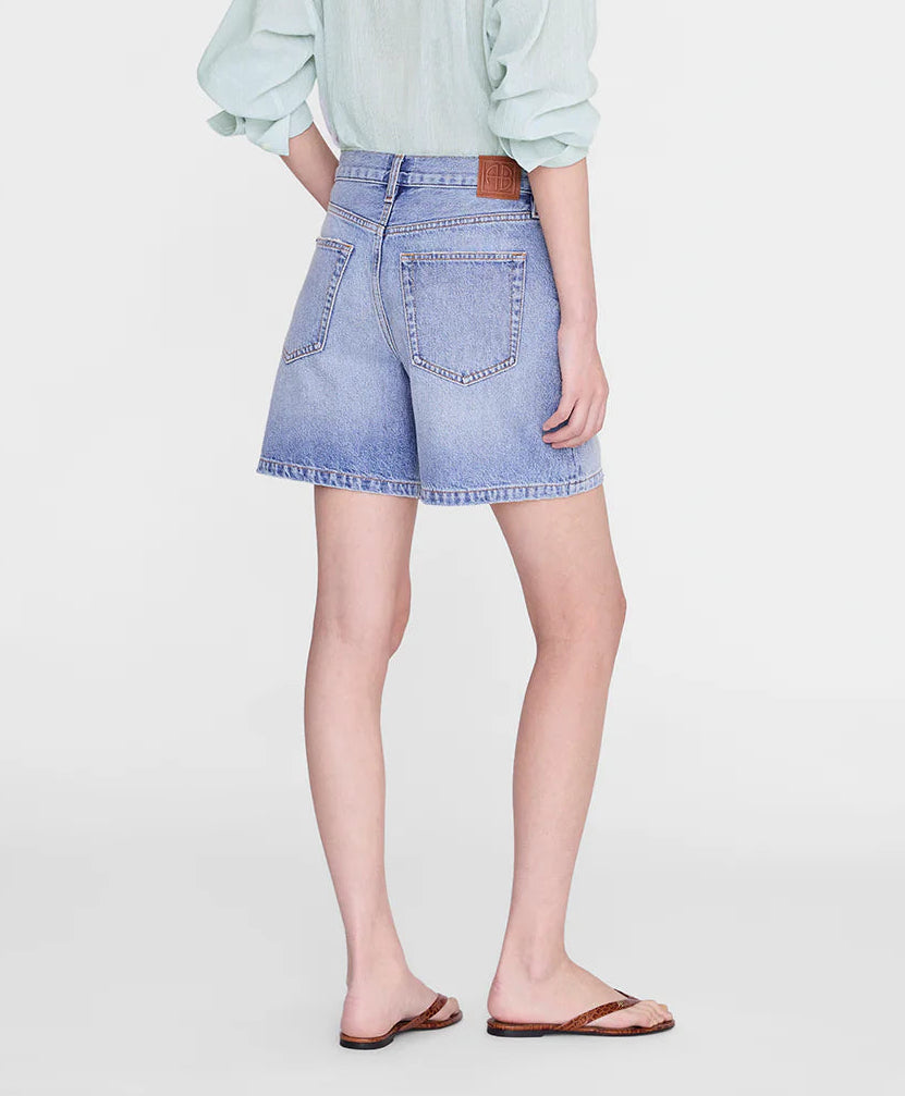 Wearing the Anine Bing Delaney Short in light blue—relaxed fit, high-rise waist, and wide leg opening—with a light long-sleeve top and brown sandals, this look stands out against a plain background.