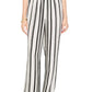 A person wears the Elain Pant Monogram by Anine Bing in an ivory and black stripe cupro blend, styled with a white top, black shoes, and a gold bracelet.