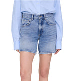 A person is shown from torso to upper legs wearing the Anine Bing Heath Short, high-waisted vintage blue wash denim baggy shorts, paired with a light blue long-sleeve shirt tucked in.