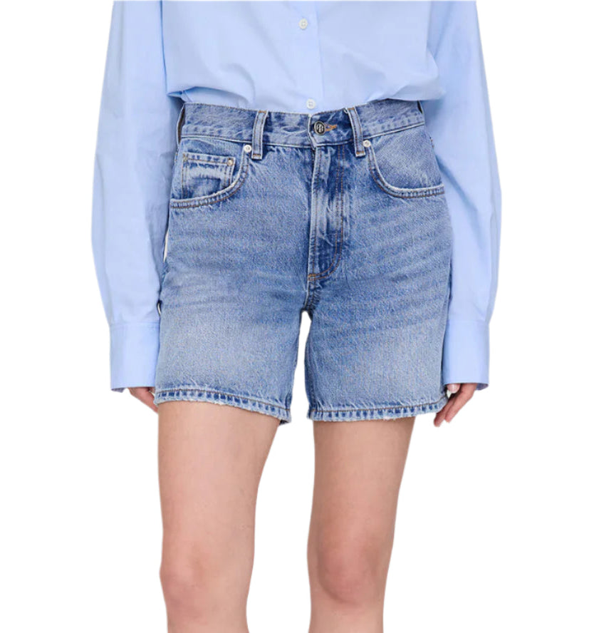 A person is shown from torso to upper legs wearing the Anine Bing Heath Short, high-waisted vintage blue wash denim baggy shorts, paired with a light blue long-sleeve shirt tucked in.