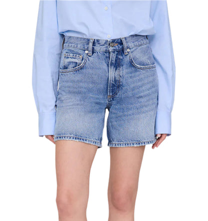 A person is shown from torso to upper legs wearing the Anine Bing Heath Short, high-waisted vintage blue wash denim baggy shorts, paired with a light blue long-sleeve shirt tucked in.